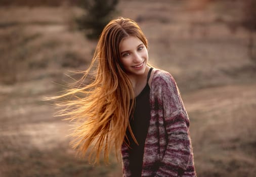 Attractive girl with sun in fluttering hair on nature background
