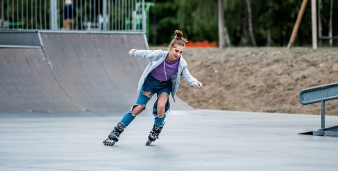 Beautiful girl roller skater riding in city park with ramp. Pretty female teenager rollerskating in casual clothes