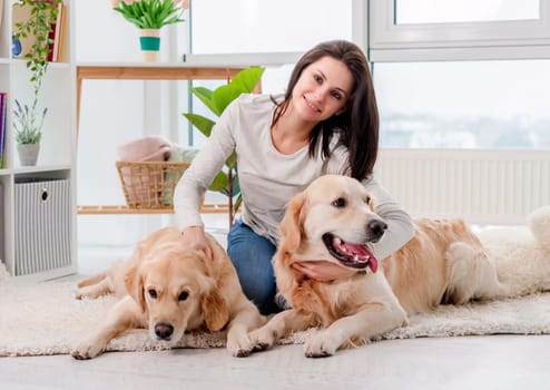 Golden retriever dogs lying on floor next to girl in light room