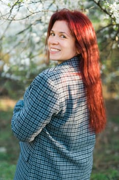 Beautiful young red hair woman near blooming spring trees alley. Youth and love, fashion and romantic and lifestyle concept