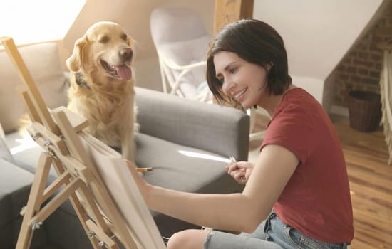 Pretty girl artist drawing sketch with golden retriever dog using pencil and canvas. Beautiful young woman painting portrait of cute doggy pet