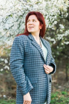 Beautiful young red hair woman near blooming spring trees alley. Youth and love, fashion and romantic and lifestyle concept