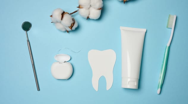 Tube with toothpaste, dental floss and medical mirror on a green background, oral hygiene. Top view