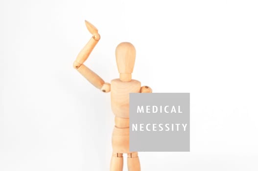 A wooden figure is holding a sign that says Medical Necessity. Concept of urgency and importance, as the figure is reaching out to the viewer with the sign