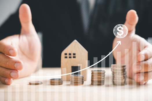Businessman holds coin stack, house wood symbolizing real estate profit. Investment growth, passive income strategy. Future budgeting, market concept, and asset building. arrow graph