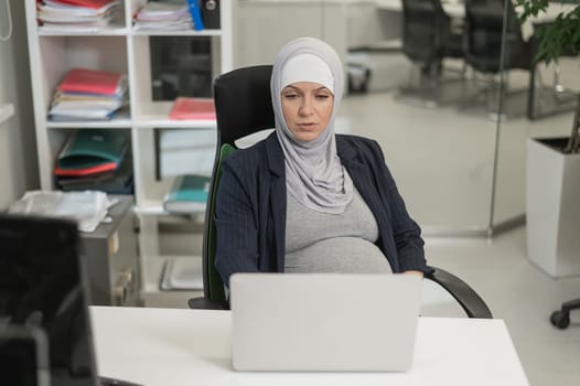 Pregnant Caucasian woman in hijab working at a computer in the office