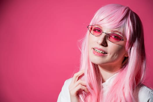 Close-up portrait of a young woman with braces in a pink wig and sunglasses on a pink background. Copy space