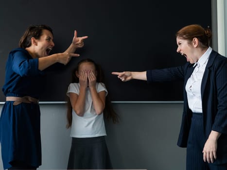 The female teacher screams at the schoolgirl and her mother standing at the blackboard