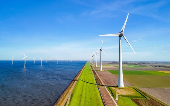 A serene scene in Flevoland, Netherlands, as a row of wind turbines elegantly spin next to the tranquil body of water in the light of spring, windmill park green energy