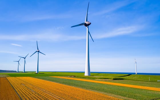 A vast expanse of green crops swaying in the breeze, with windmills towering in the distance against a clear blue sky in Flevoland, the Netherlands. zero emissions, carbon neutral