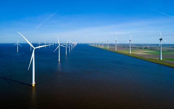 An expansive body of water in the Netherlands Flevoland is dotted with numerous towering windmills, gracefully capturing the winds energy on a breezy Spring day. windmill turbines