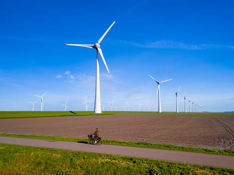A man rides his electric bike down a dirt road alongside towering wind turbines on a sunny day in the Netherlands Flevoland in Spring. men on electric bicycle countryside