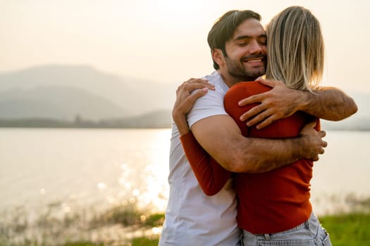 Close up Caucasian man hug with his lover woman near lake with romace and sunset light and they look happy and enjoy together.