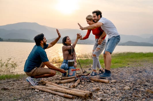 Caucasian man and woman walk and join and touch hands with Asian friends for party and camping near lake with sunset.