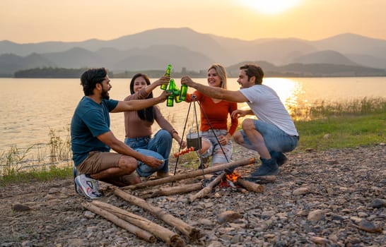 Group of men and woman friends with multi-ethnic enjoy in party and cheers action with surrounded by fire and they look happy to join together in public park near lake and sunset.