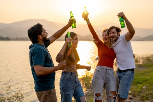 Group of friends with multi-ethnic enjoy with dancing and hold bottle of drinking in public park near the lake with sunset light.