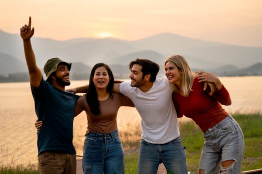 Group of friends with multi-ethnic hug together and stand in front of sunset light near lak of public park with happiness.