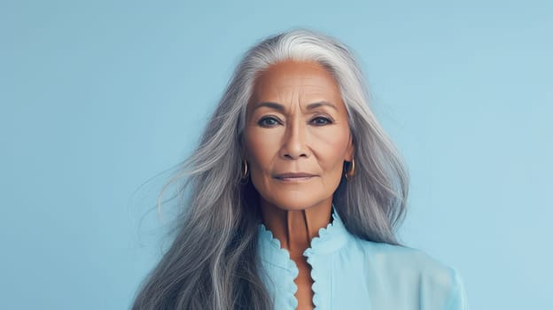 Elegant, elderly, chic Latino, Spain woman with gray long hair and perfect skin, on a blue background, banner. Advertising of cosmetic products, spa treatments, shampoos and hair care products, dentistry and medicine, perfumes and cosmetology women