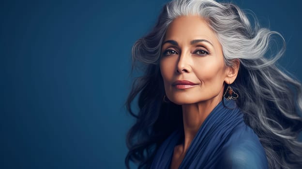 Elegant, elderly, chic latino, Spain woman with gray long hair and perfect skin, blue background, banner. Advertising of cosmetic products, spa treatments, shampoos and hair care products, dentistry and medicine, perfumes and cosmetology for women