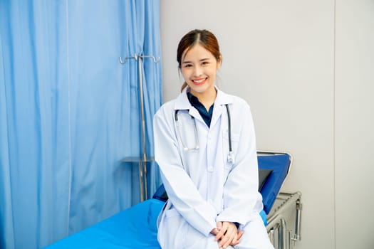 Portrait of beautiful woman doctor sit on hospital bed with stethoscope and look at camera with smiling in emergency toom.