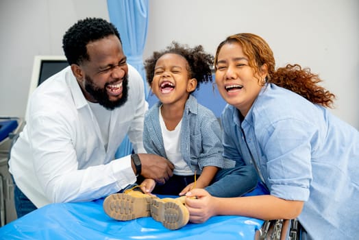 Portrait of African American father laugh with little girl and Asian wife and stay in area of emergency room and they look happiness.