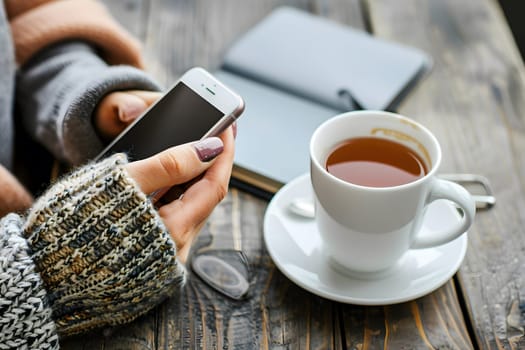 Close-up of woman's hands holding a smartphone and a cup of tea, symbolizing comfort, leisure, and digital disconnection.
