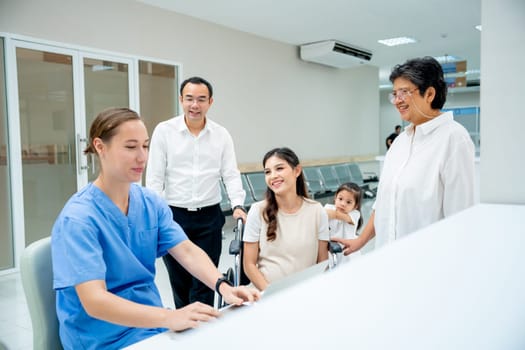 Asian family with young family and senior woman discuss with nurse or doctor in hallway of hospital.