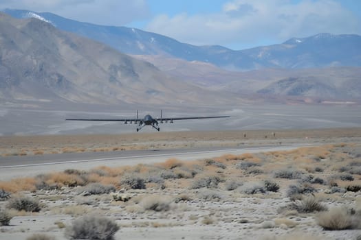 Solar-paneled military drone makes its approach for a landing in a vast desert environment with a picturesque mountain range in background during daylight.