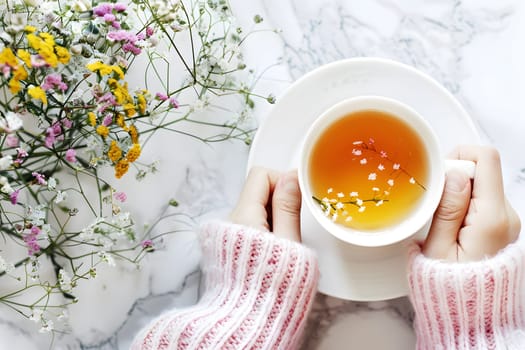 Overhead view of hands holding a cup of tea surrounded by vibrant wildflowers, signaling relaxation and a fresh start to the day.