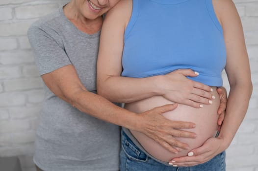 An elderly woman touches the belly of her pregnant daughter. Close-up