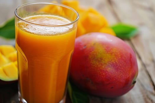 Vibrant orange mango juice served in clear glass, with ripe mango fruit and slices on a rustic wooden background, symbolizing freshness and natural taste.