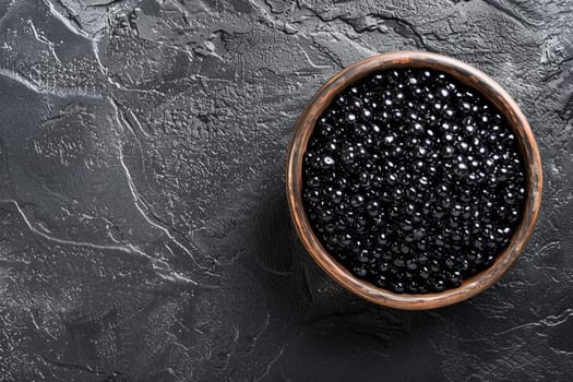 Top view of premium black sturgeon caviar in rustic wooden bowl placed on dark textured background, symbolizing luxury and gourmet dining.