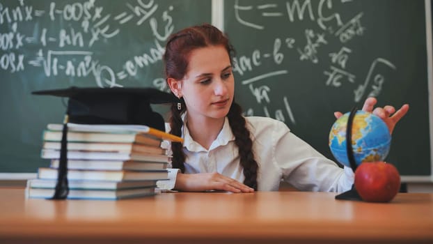 A red-haired high school senior poses against a backdrop of books, a globe and a graduation cap