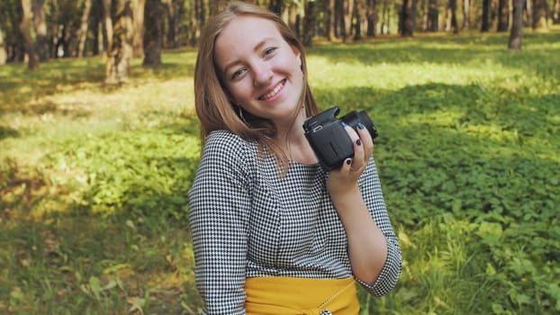 A young girl photographer with a camera poses in the park