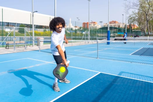 Man with afro hairstyle playing pickleball in an outdoor blue court in a sunny day