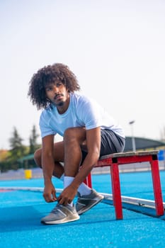 Vertical portrait of a concentrated young african american running getting ready to train tying her shoelaces in a blue outdoor running track