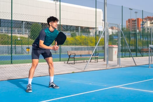Full length photo with copy space of a sportive man playing pickleball in an outdoor blue court