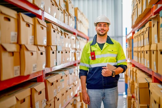 Portrait of professional warehouse worker stand with holding tablet and look at camera in workplace area between shelves with cardbox of product.