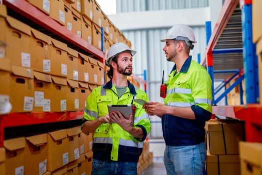 Two professional warehouse workers stand between shelves of products and discuss together about work in workplace area. The concept of good system support the worker for stock and shipment industry.