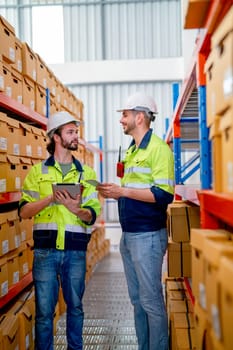Two professional warehouse workers stand between shelves of products and discuss together about work in workplace area. The concept of good system support the worker for stock and shipment industry.