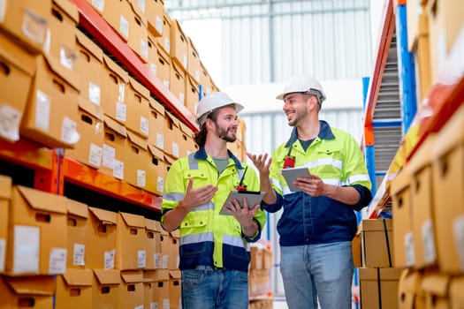 Two professional warehouse worker men hold tablet and discuss about work together also stay between shelves with product in workplace and they look happy.