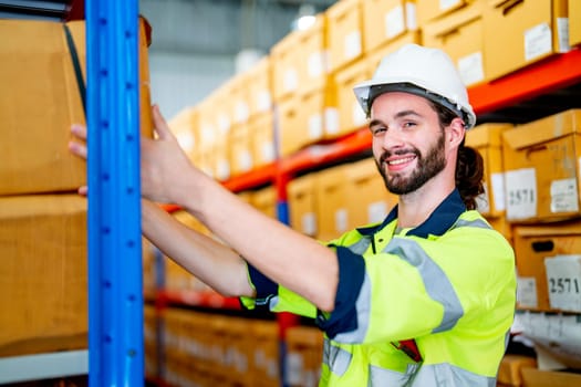 Close up smart warehouse worker man hold box on shelves also look at camera with smiling stay in workplace area.
