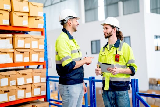 Two professional warehouse worker men hold tablet and discuss about work together also stay in front of shelves with product boxes.