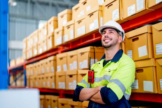 Smart professional warehouse worker stand and lean against the product boxes on shelves and also look at upper direction with smiling in workplace.