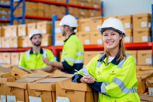 Beautiful young warehouse woman worker stand in front of her co-worker men and look at camera with smiling.