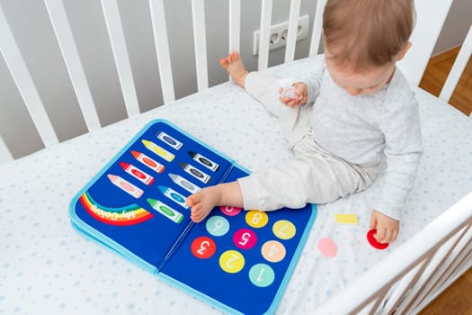 A happy baby is sitting in a crib playing with a felt board. Its a joyful leisure event