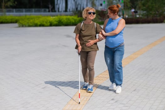 Caucasian pregnant woman leading blind elderly lady outdoors