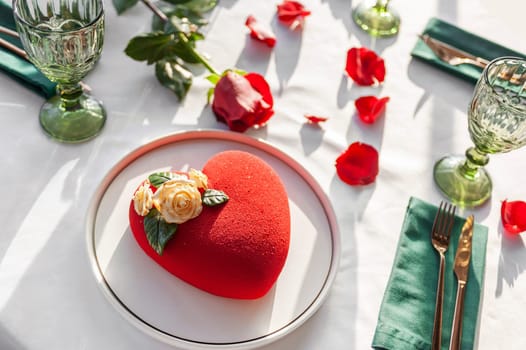 Heart Shaped Red Velvet Valentine's Day Cake on a white tablecloth with a red rose and rose petals in a restaurant. High quality photo