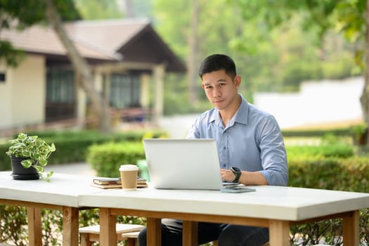 Adult businessman sitting at outdoor table and working on laptop computer.