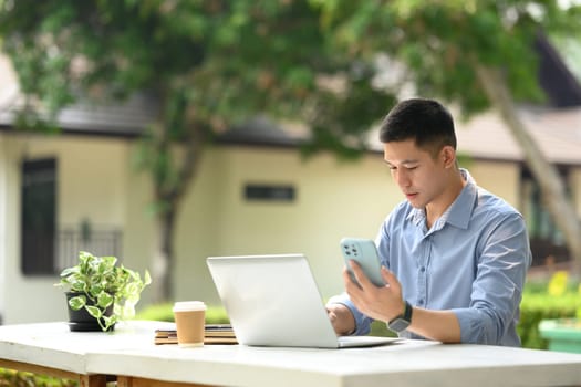 Millennial male entrepreneur holding mobile phone and working on laptop at outdoor.